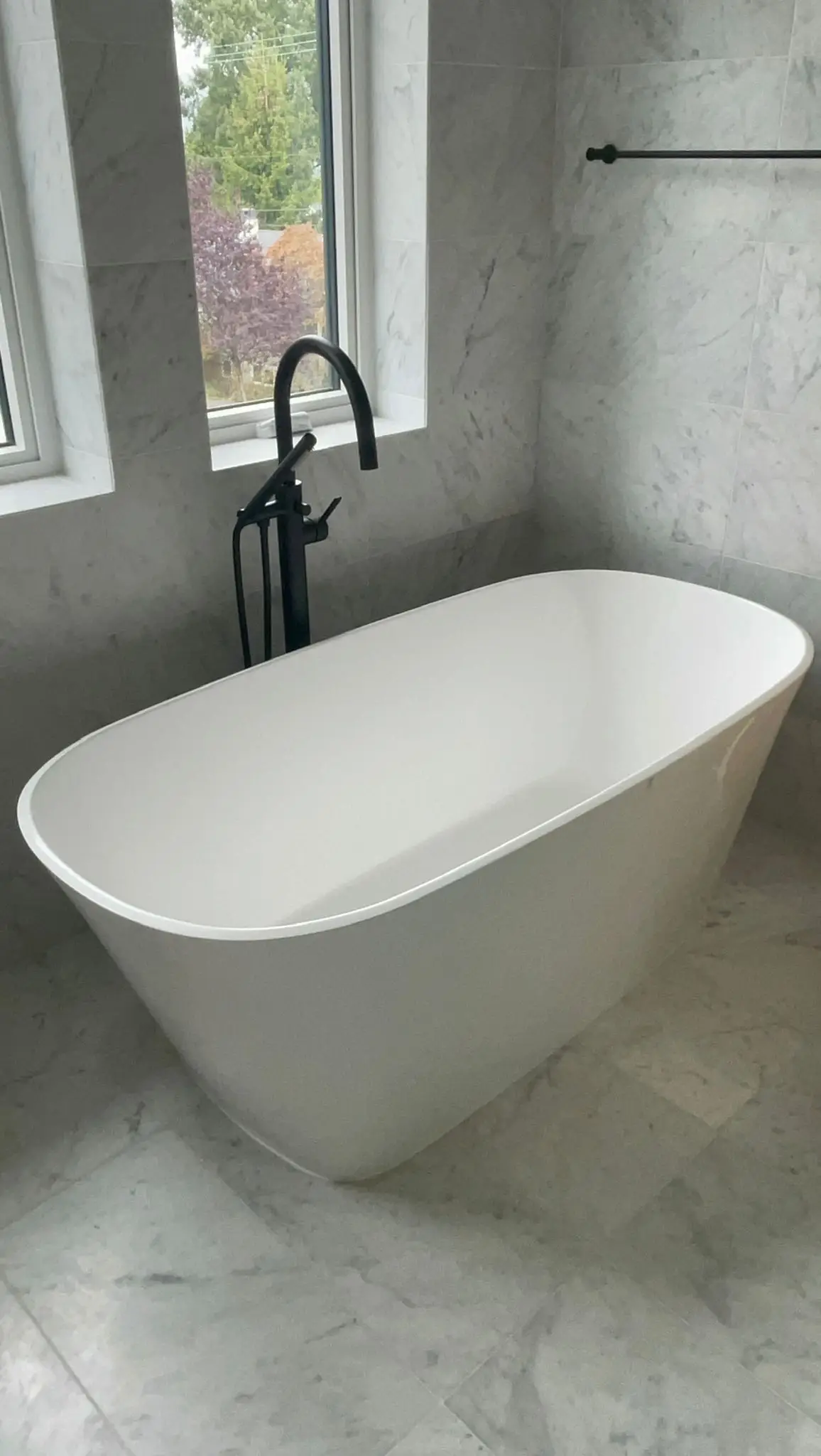 A freestanding bath against marble, with the filler standing clear of the tub.