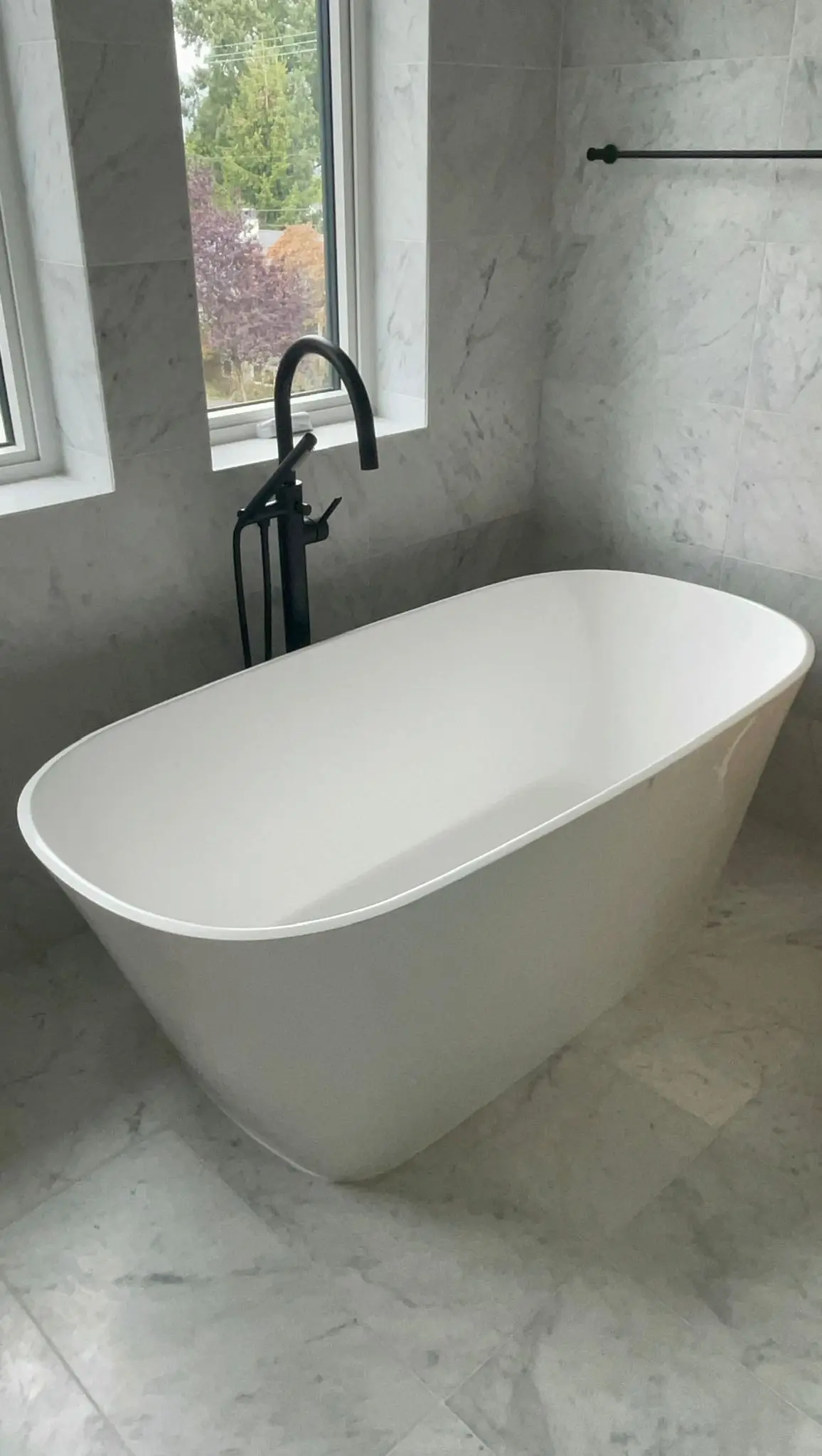 A freestanding bath against marble, with the filler standing clear of the tub.