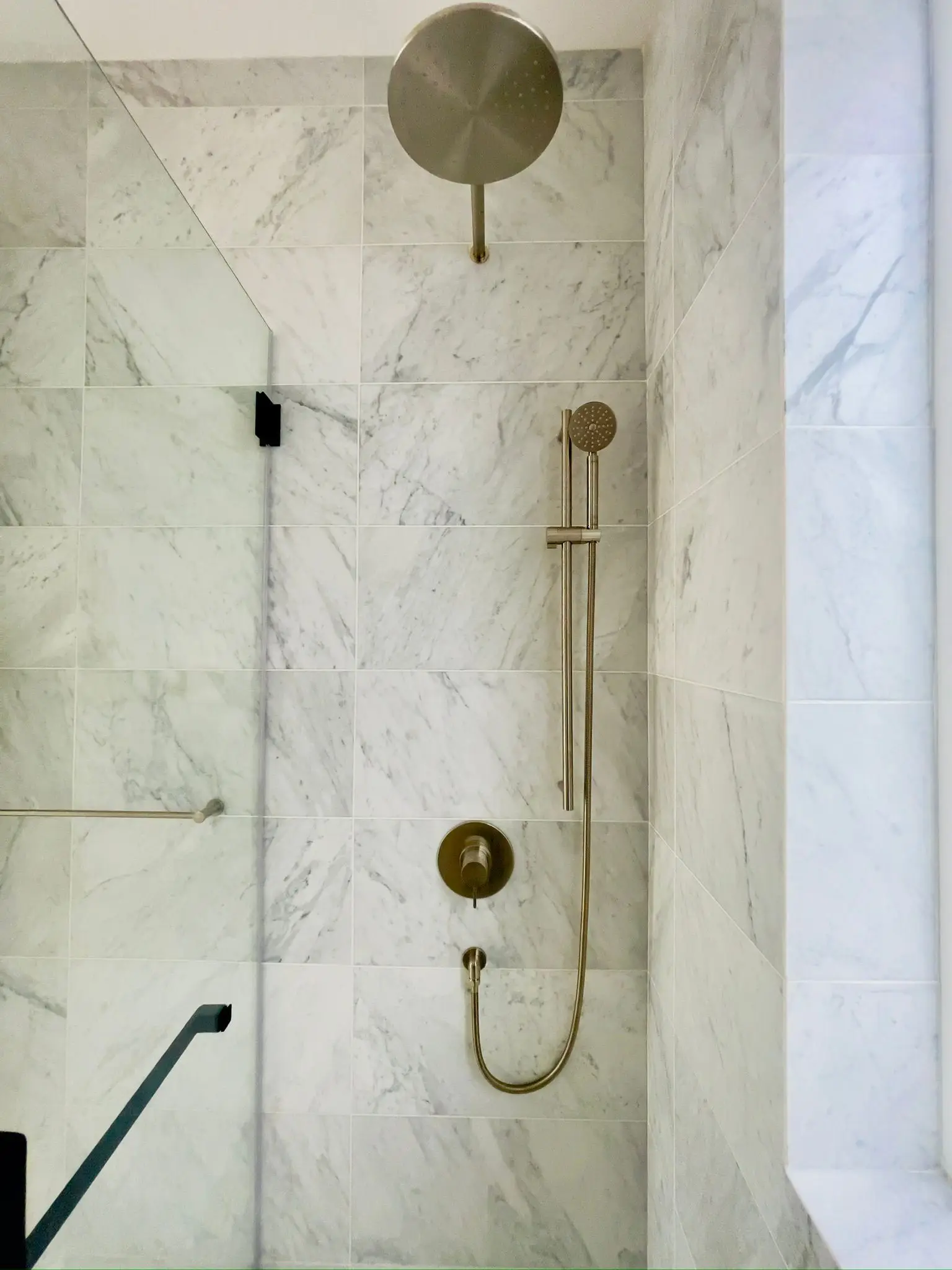 A marble shower with a brass rainhead and a handset on a slide rail.
