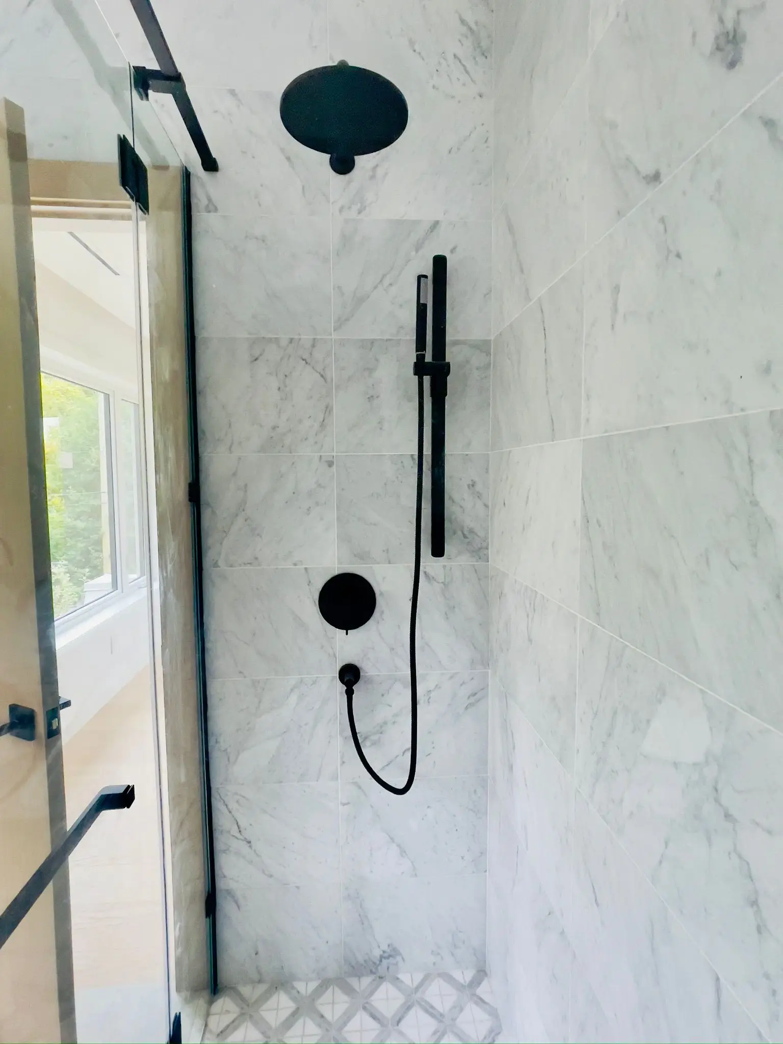 A walk-in shower in marble with a black rainhead, handset and thermostatic valve.