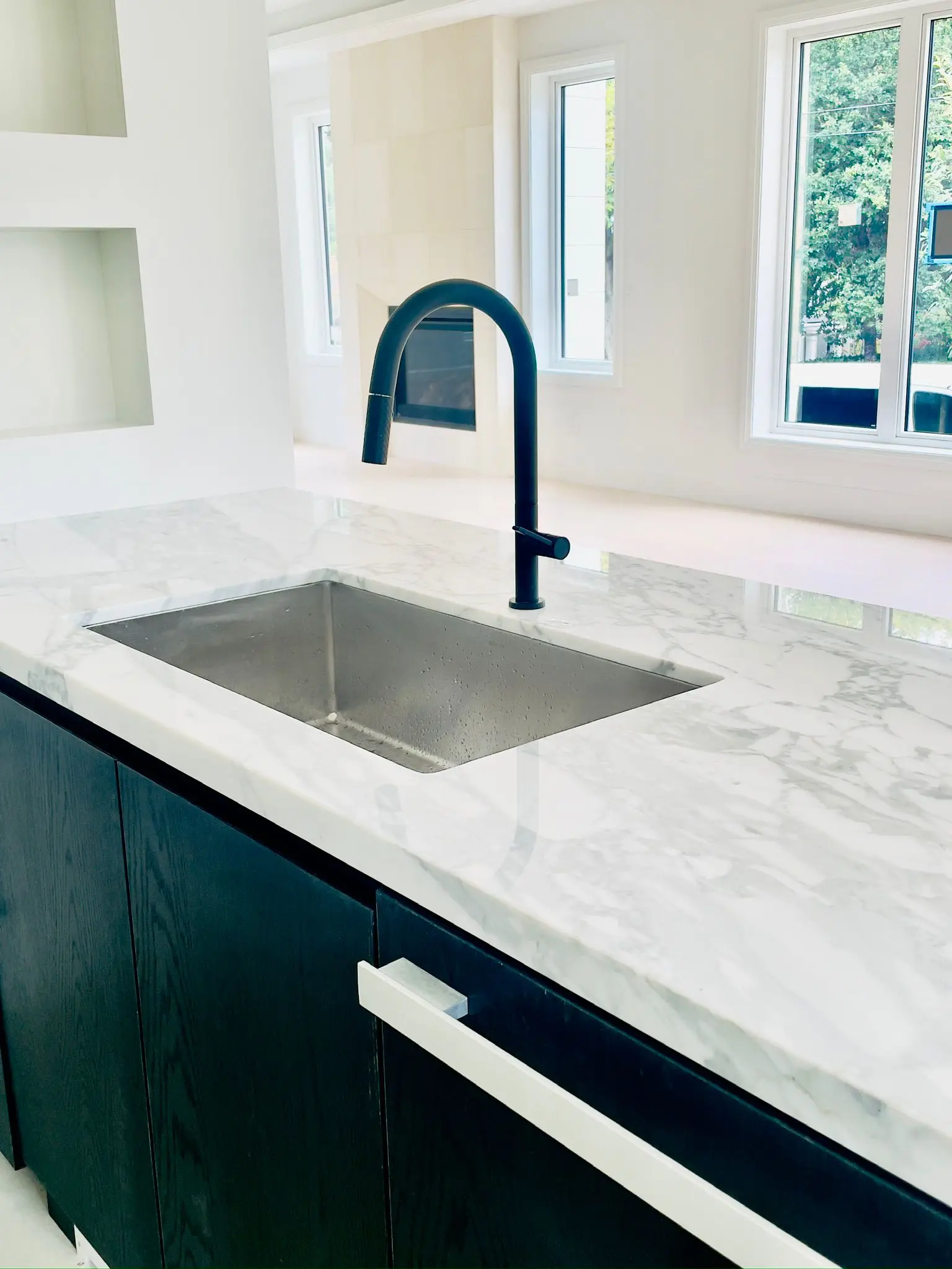 A stainless kitchen sink undermounted in marble with a black gooseneck tap.