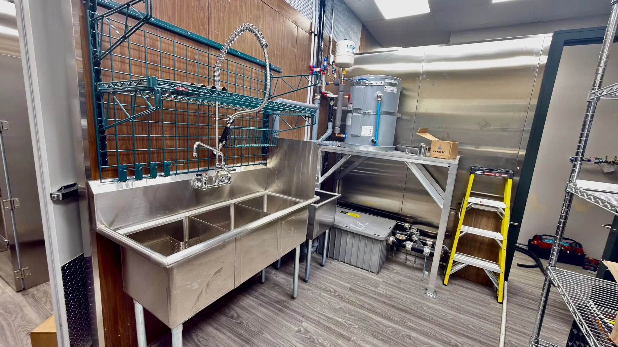 A three-compartment sink, pre-rinse and water heater installed in a restaurant kitchen.
