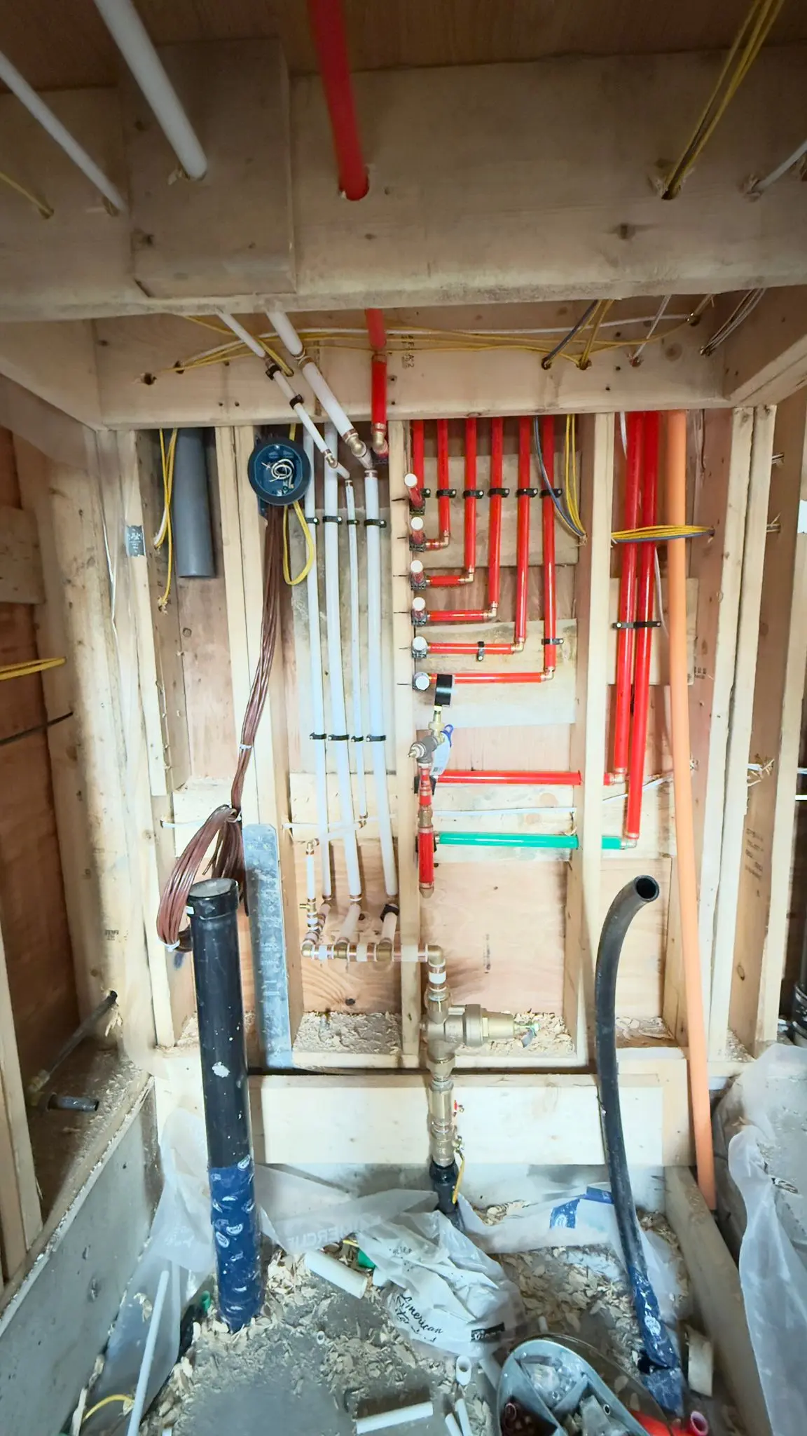 A pressure gauge and isolation valves on a supply rough-in beside the drainage stack.