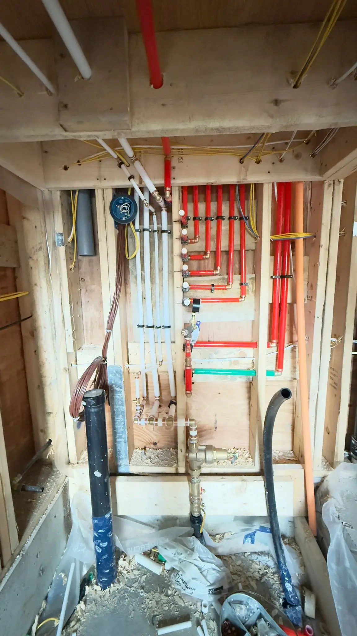 A pressure gauge and isolation valves on a supply rough-in beside the drainage stack.