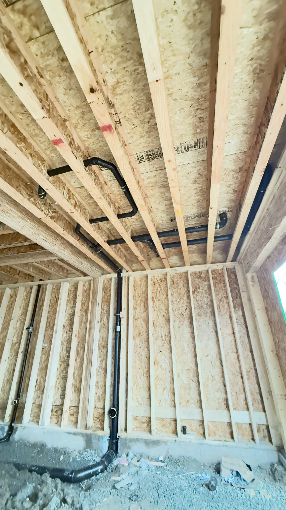 A black ABS vent line carried through the ceiling joists of a new build.