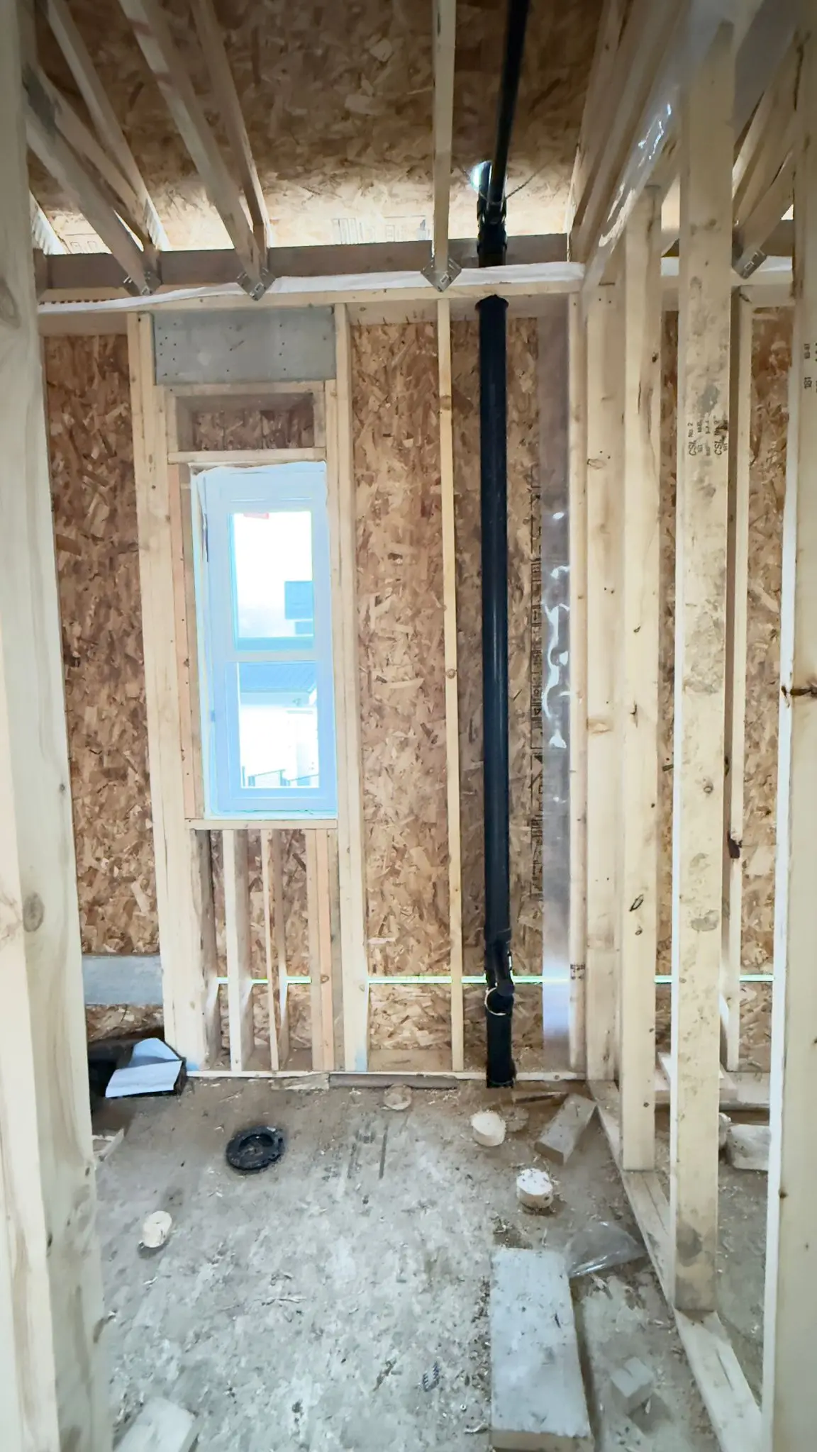 A soil stack run floor to ceiling through the framing beside a window.