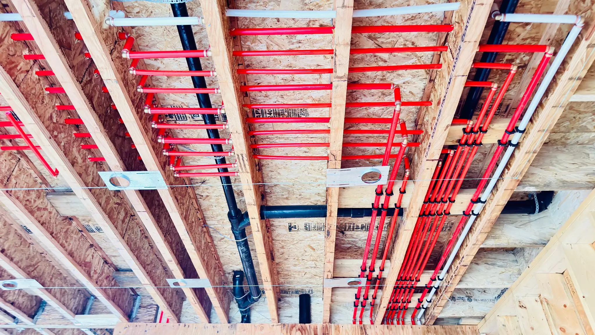 Red PEX supply and black drainage run together through the floor joists.