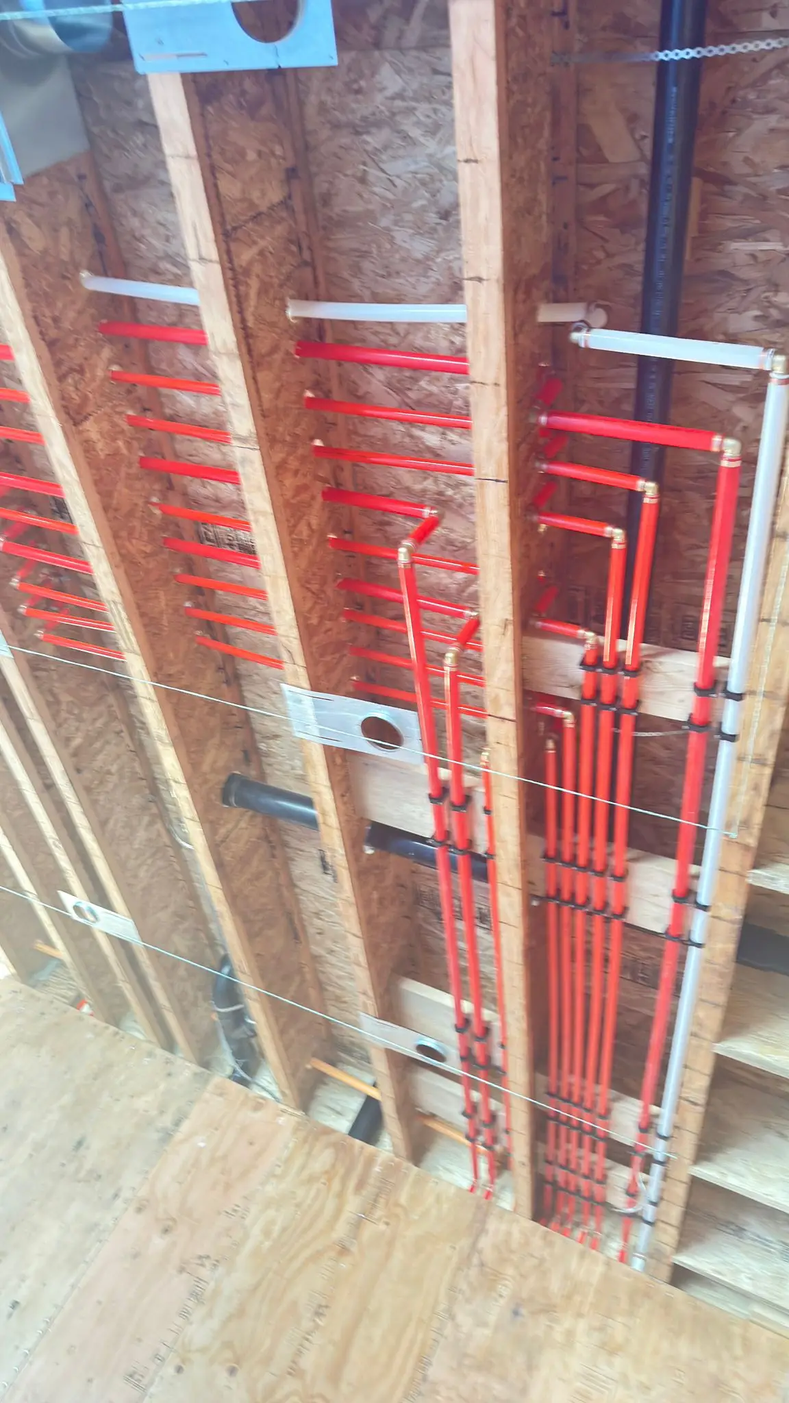 Red PEX supply lines carried through the ceiling joists of a new build.