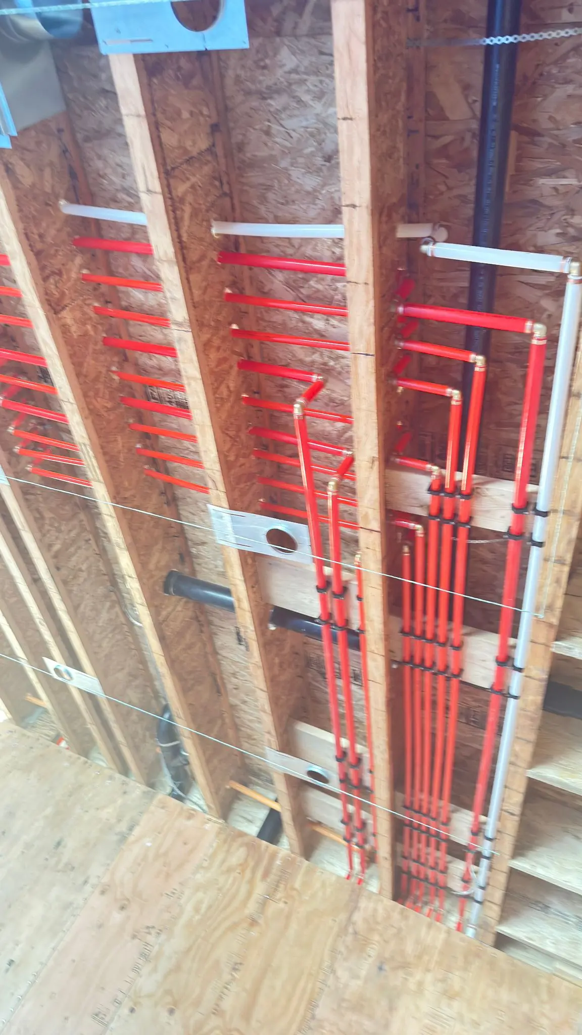 Red PEX supply lines carried through the ceiling joists of a new build.