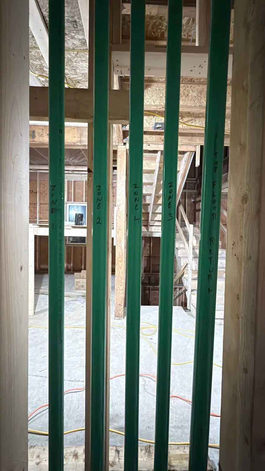 Labelled radiant heating risers standing in an open framed bay.