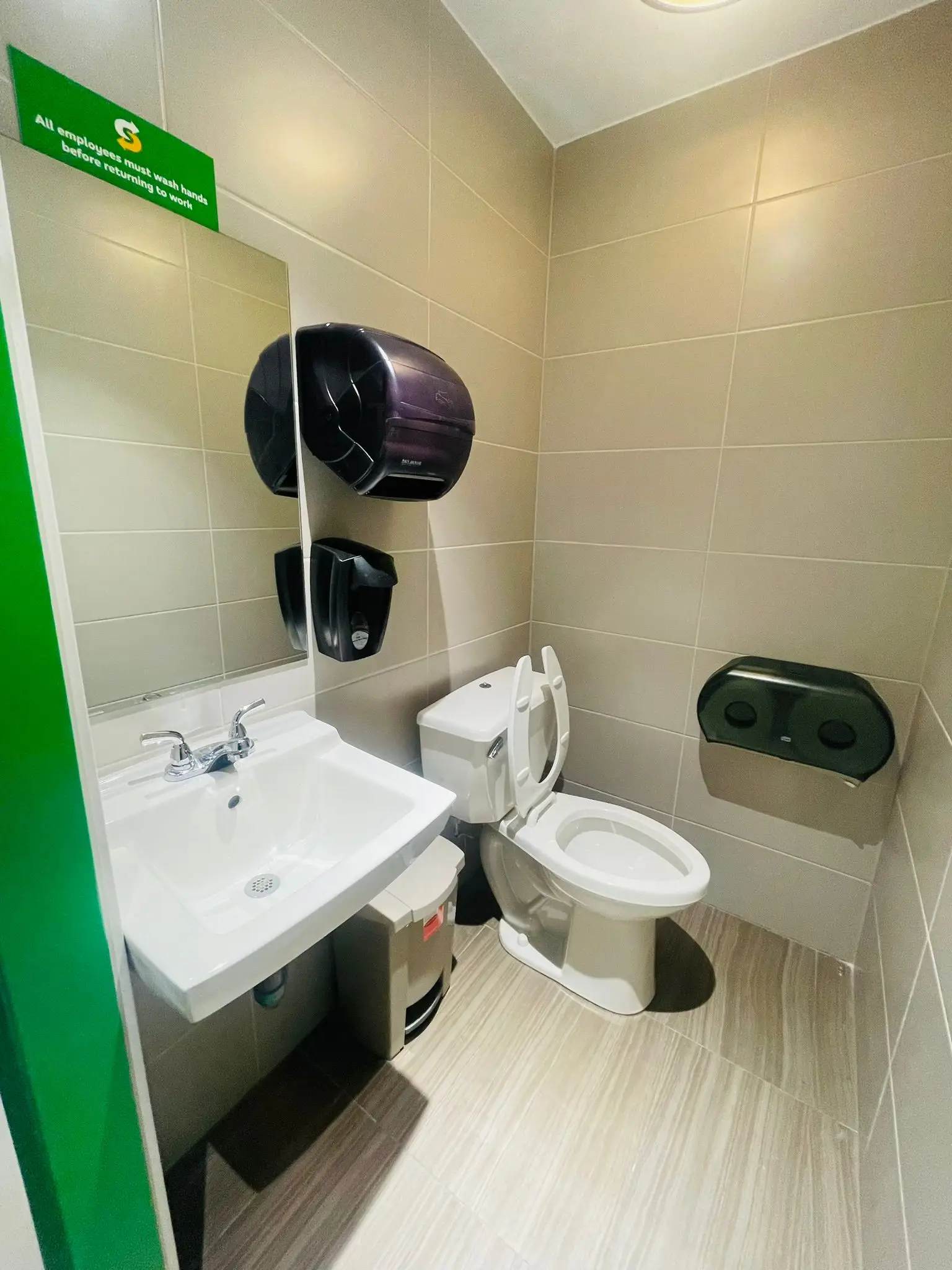 A commercial washroom with a wall-hung basin and dispensers.